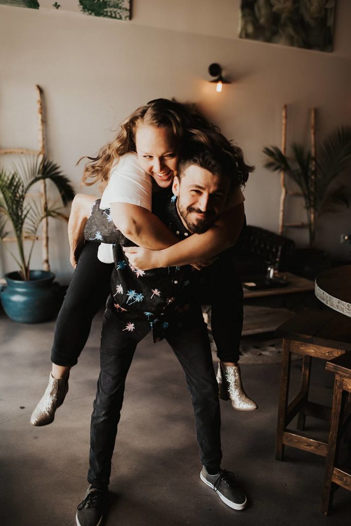 Couple giving piggy back ride during engagement session at brewery