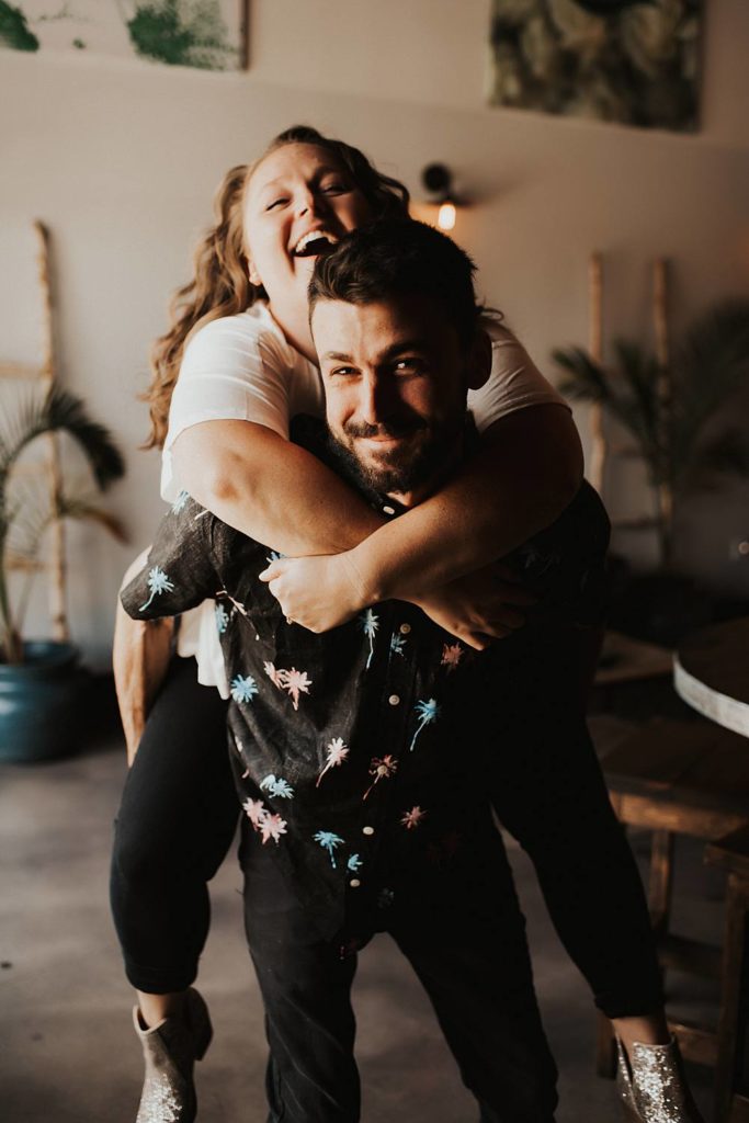 Couple giving piggy back ride during engagement session at brewery