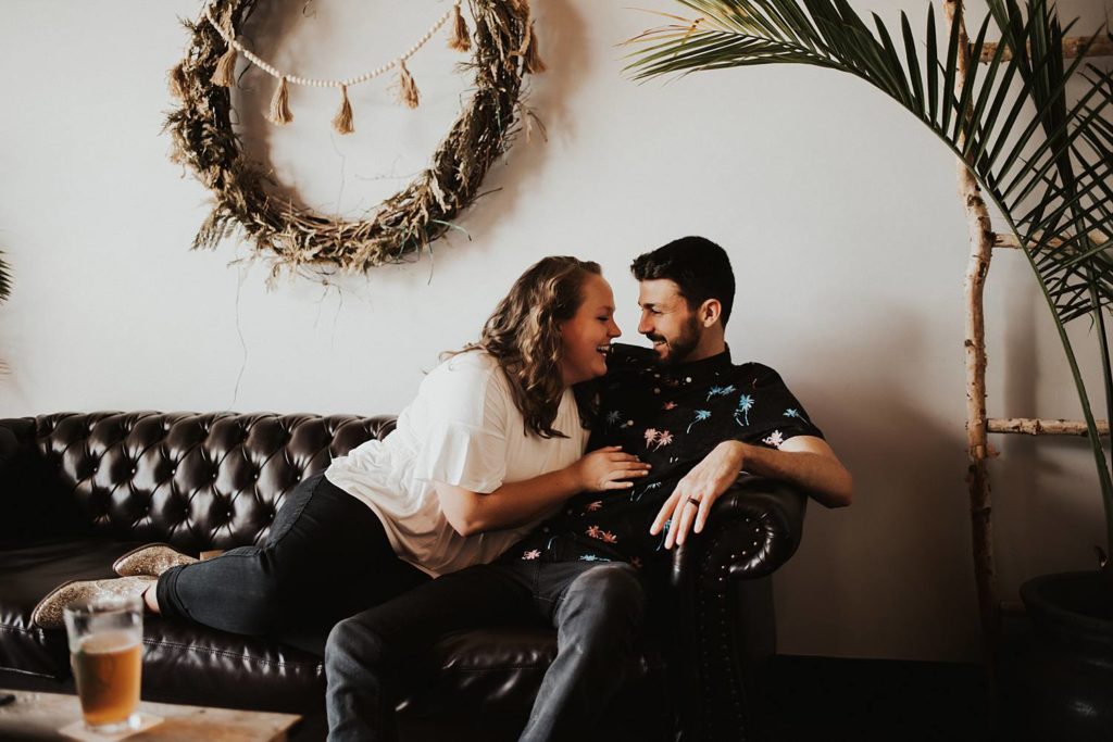 Couple sitting on couch laughing during engagement session at brewery