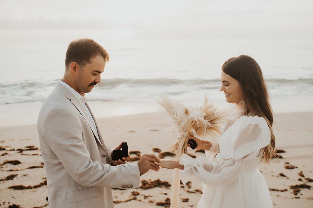 Bride and groom exchanging rings on beach