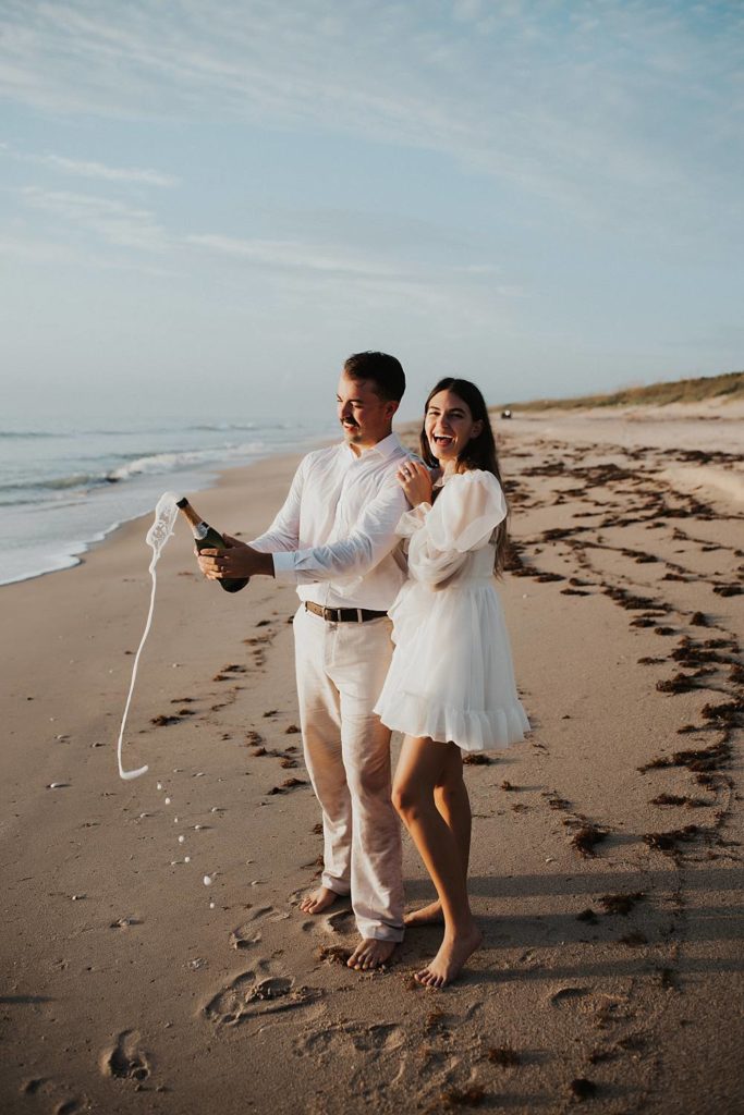 Bride and groom popping champagne on beach