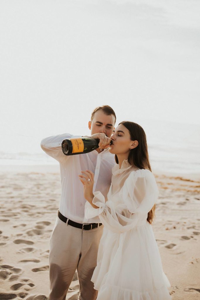 Bride drinking champagne on the beach