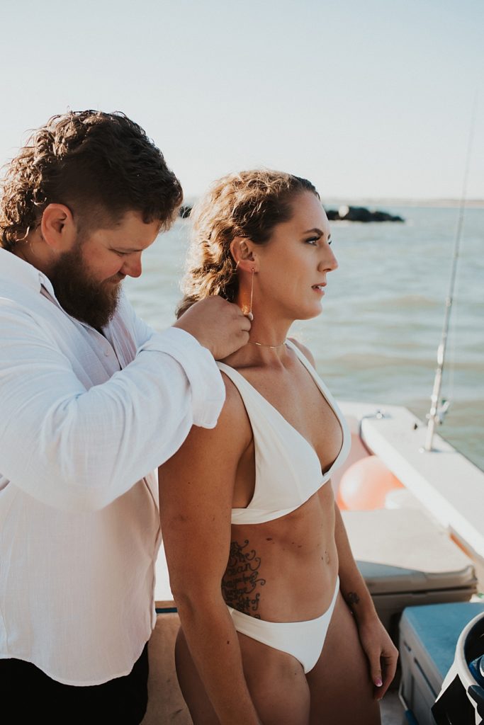 Groom putting on necklace for bride in bikini