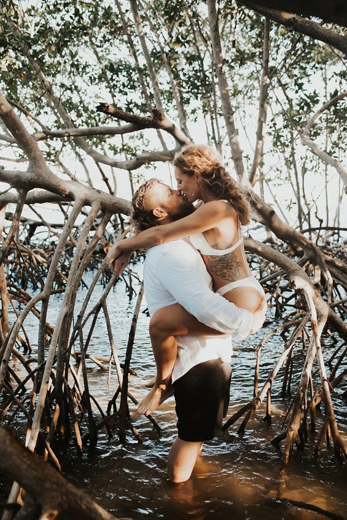 Groom lifting bride in white bikini in mangrove trees