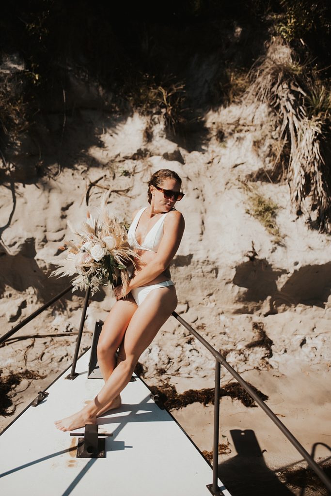 Bride in bikini with dried floral bouquet on front of boat