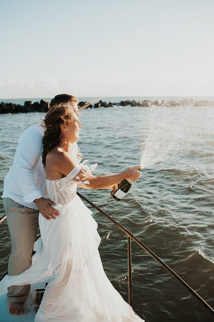 Bride and groom popping champagne on front of boat