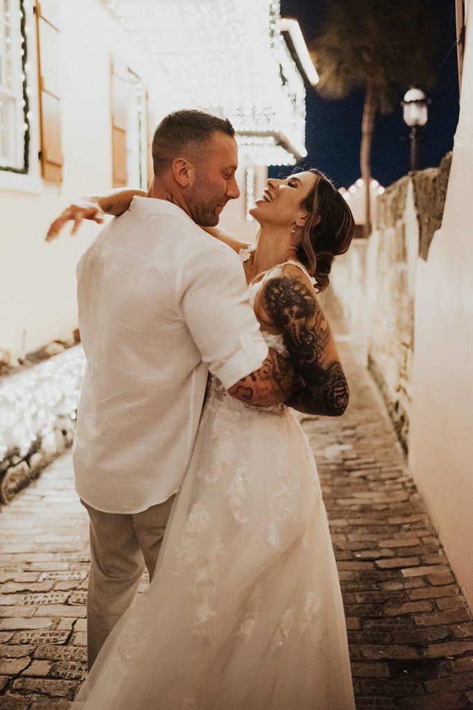 Bride and groom laughing as groom pulls her in for a kiss in an alleyway