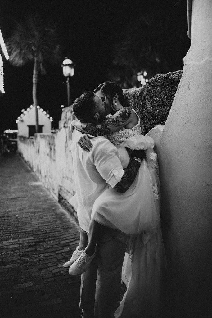 Groom picking up bride and pushing her against a wall in an alleyway