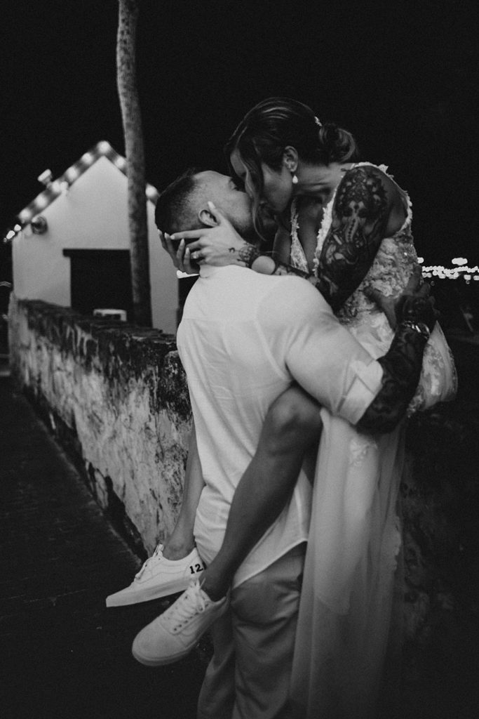 Bride sitting on a ledge kissing groom