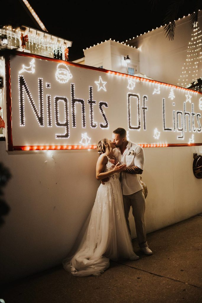 Bride and groom kissing in front of night of lights sign