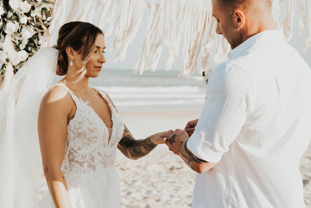 Groom placing ring on brides finger at beach wedding