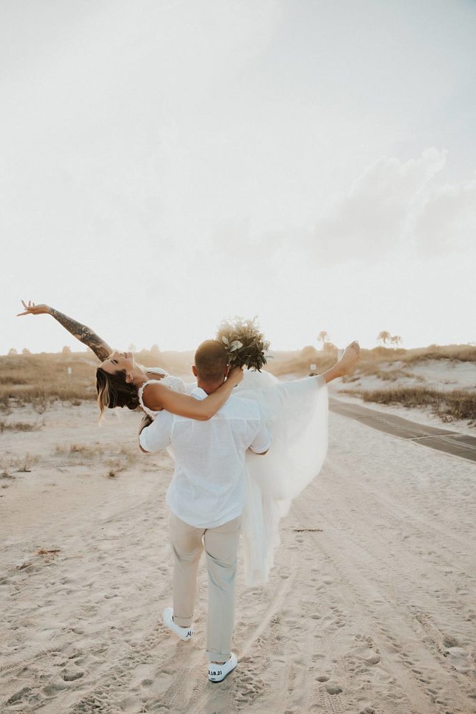 Groom carrying bride away on Saint Anastasia beach