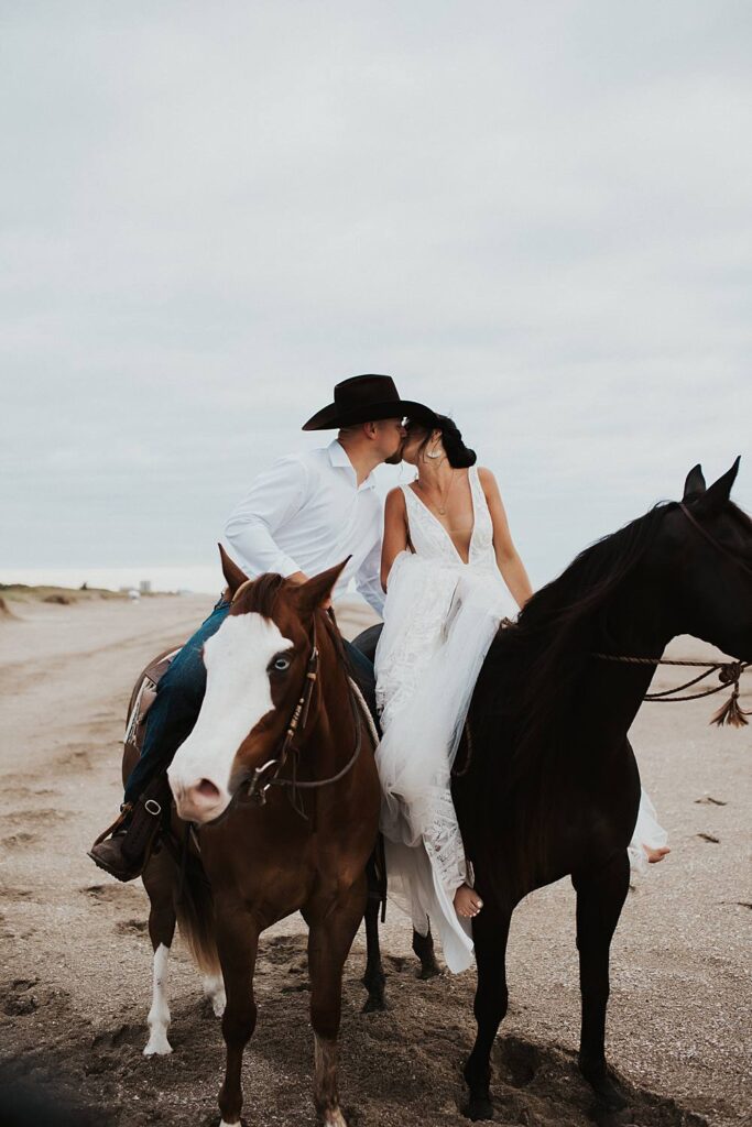 Bride and groom kissing while sitting on their horses at the beach in Florida for their elopement