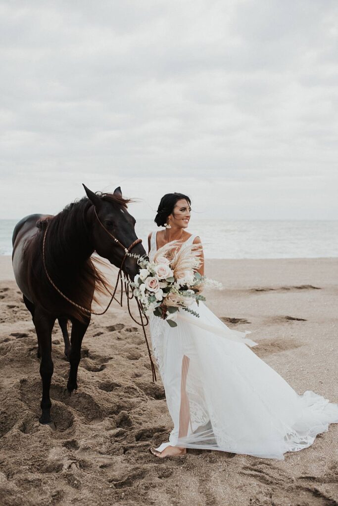 Bride walking horse with neutral floral bouquet at the beach
