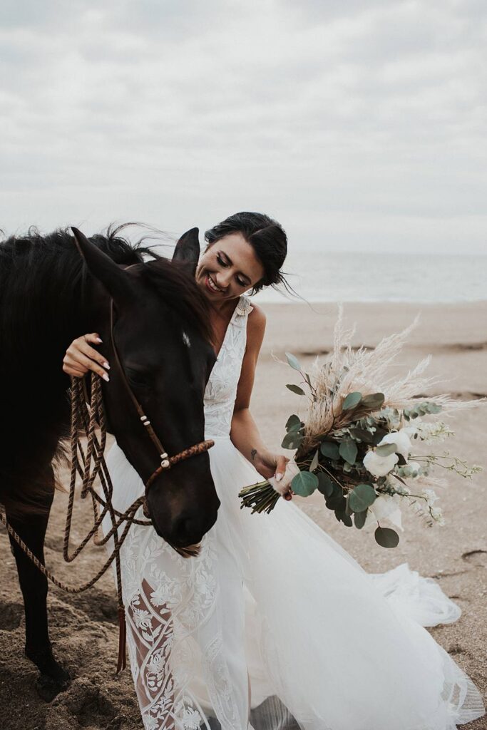 Bride walking horse with neutral floral bouquet at the beach