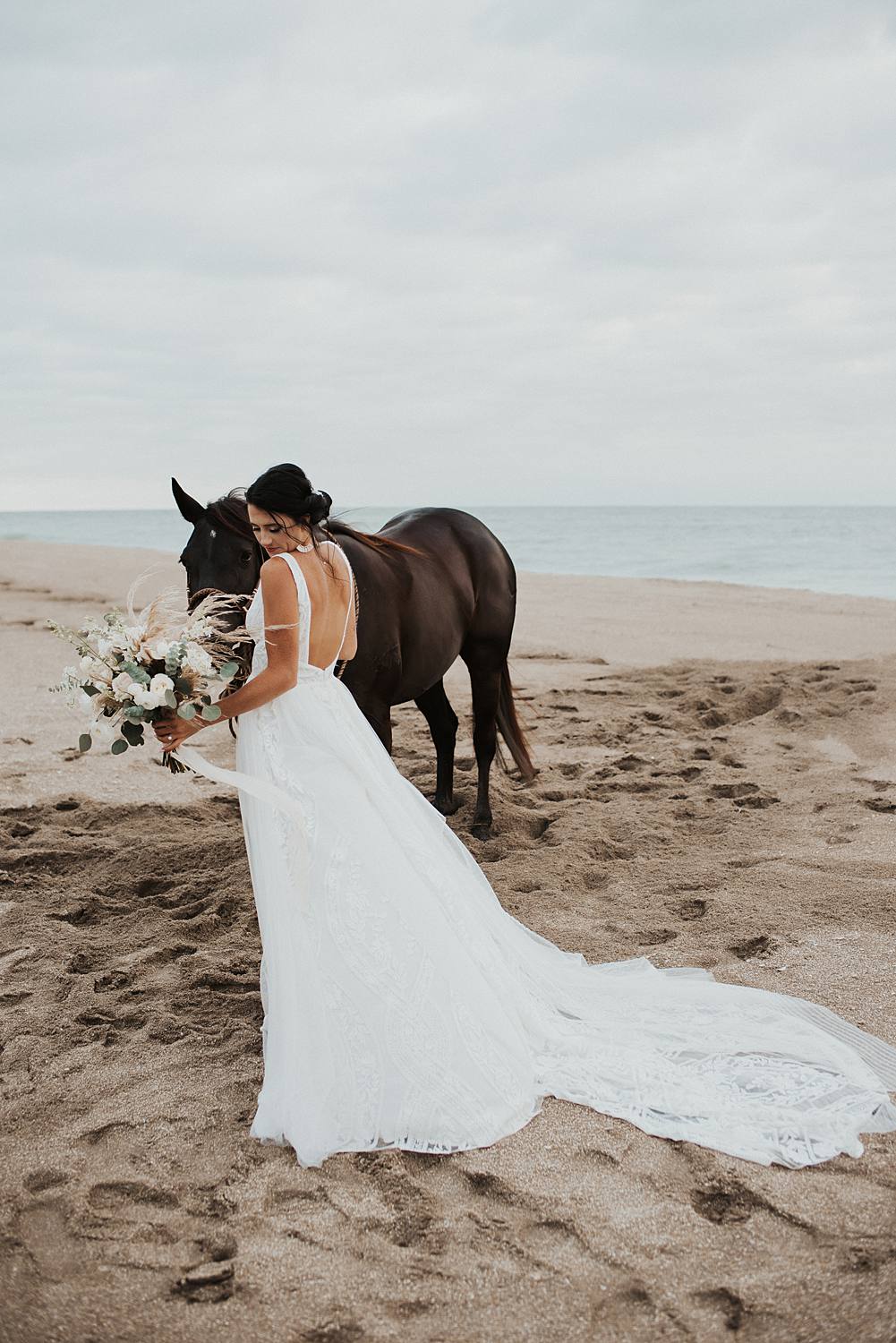 Bride walking horse with neutral floral bouquet at the beach