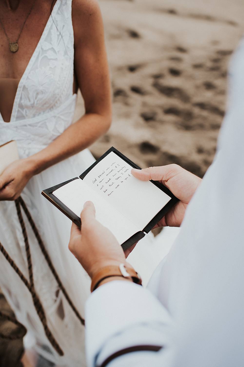 Groom reading vows from vow book at the beach