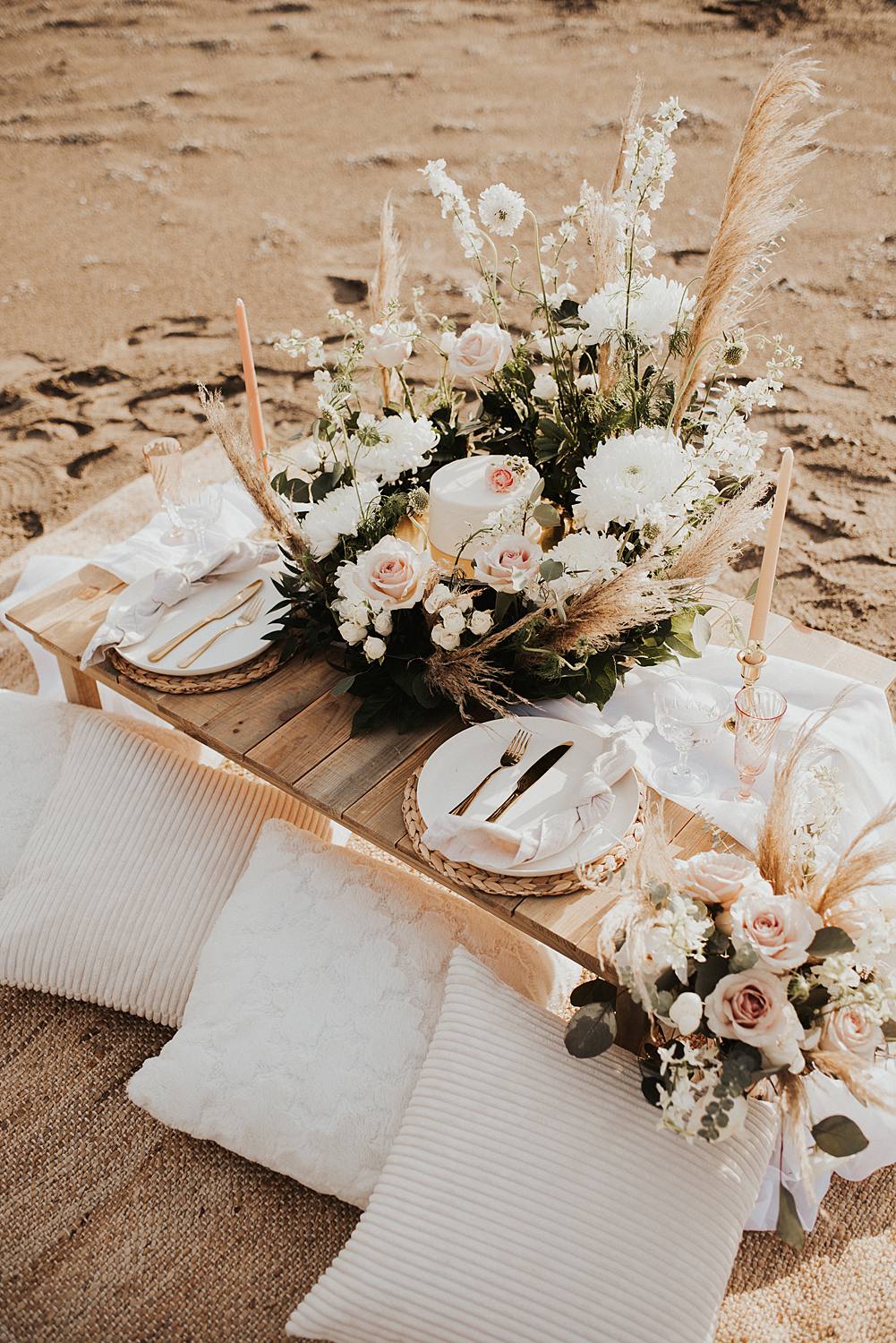 Luxury picnic on Florida beach with pillow seats and floral meadow around cake