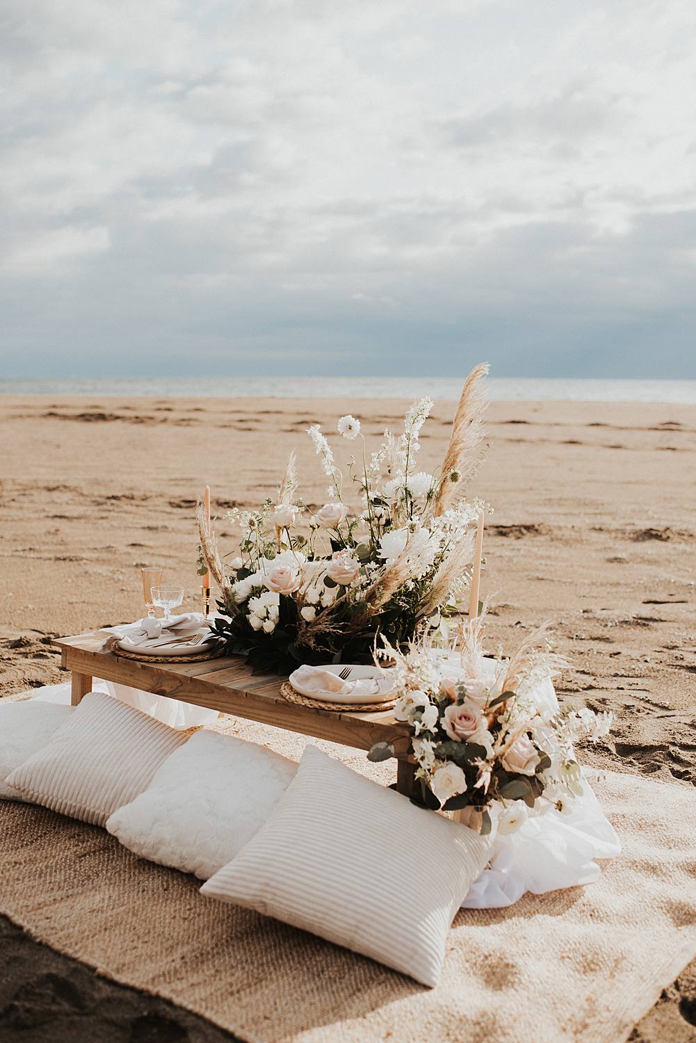 Luxury picnic on Florida beach with pillow seats and floral meadow around cake