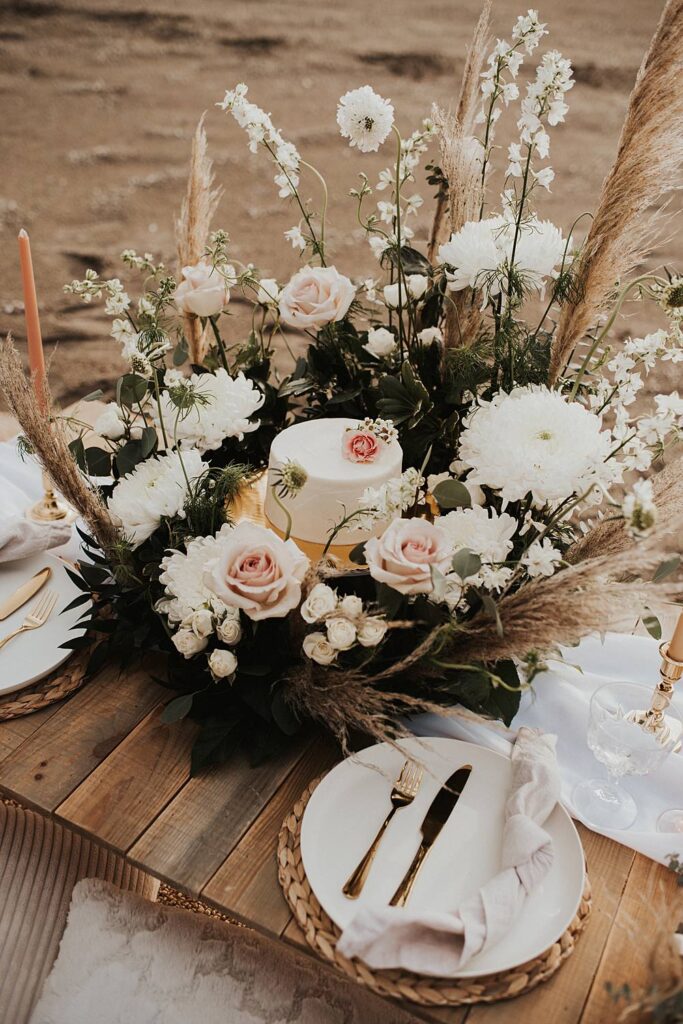Luxury picnic on Florida beach with pillow seats and floral meadow around cake