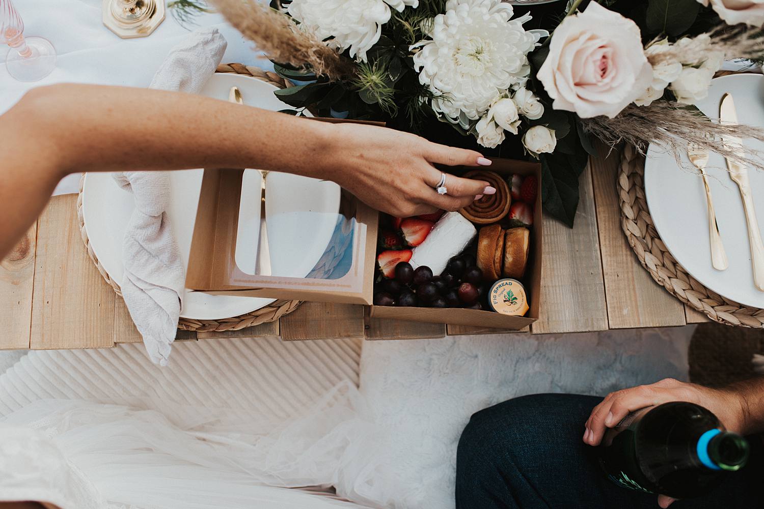 Bride picking up a strawberry from their luxury picnic on the beach