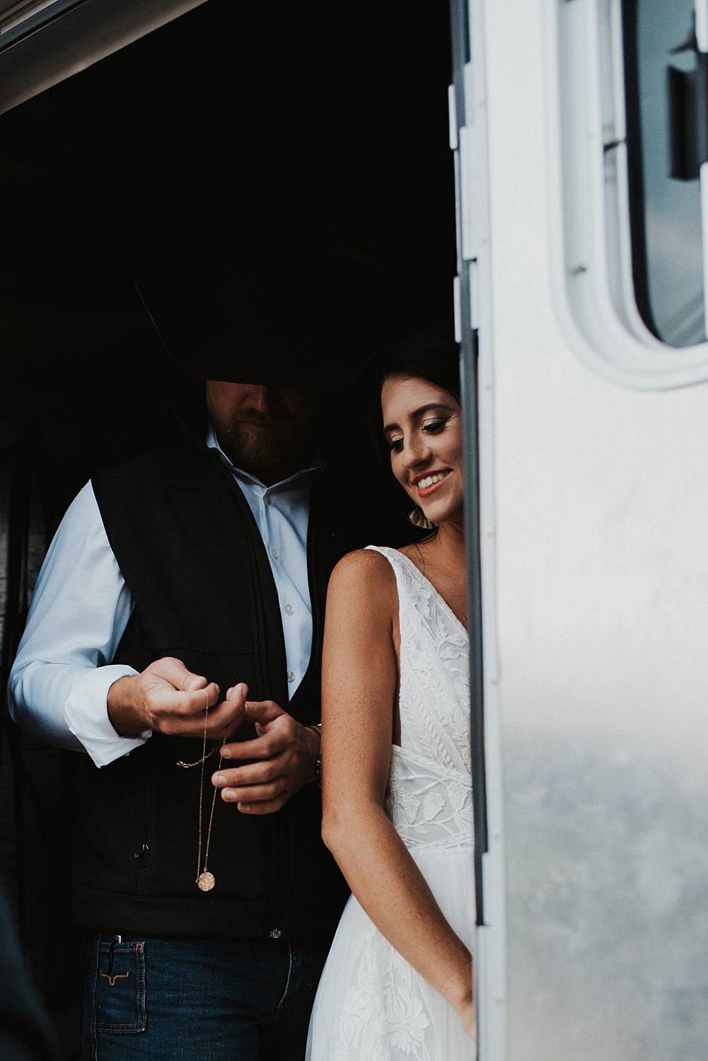 Groom helping bride put on a necklace inside of a horse trailer