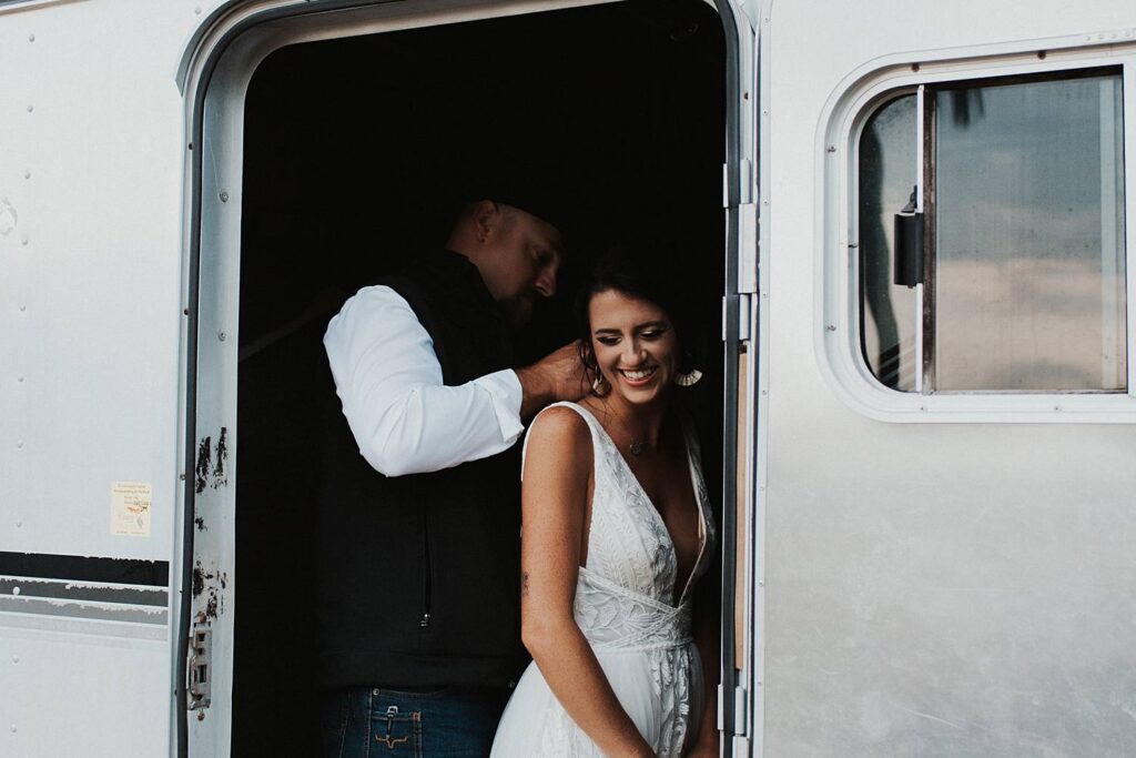 Groom helping bride put on a necklace inside of a horse trailer