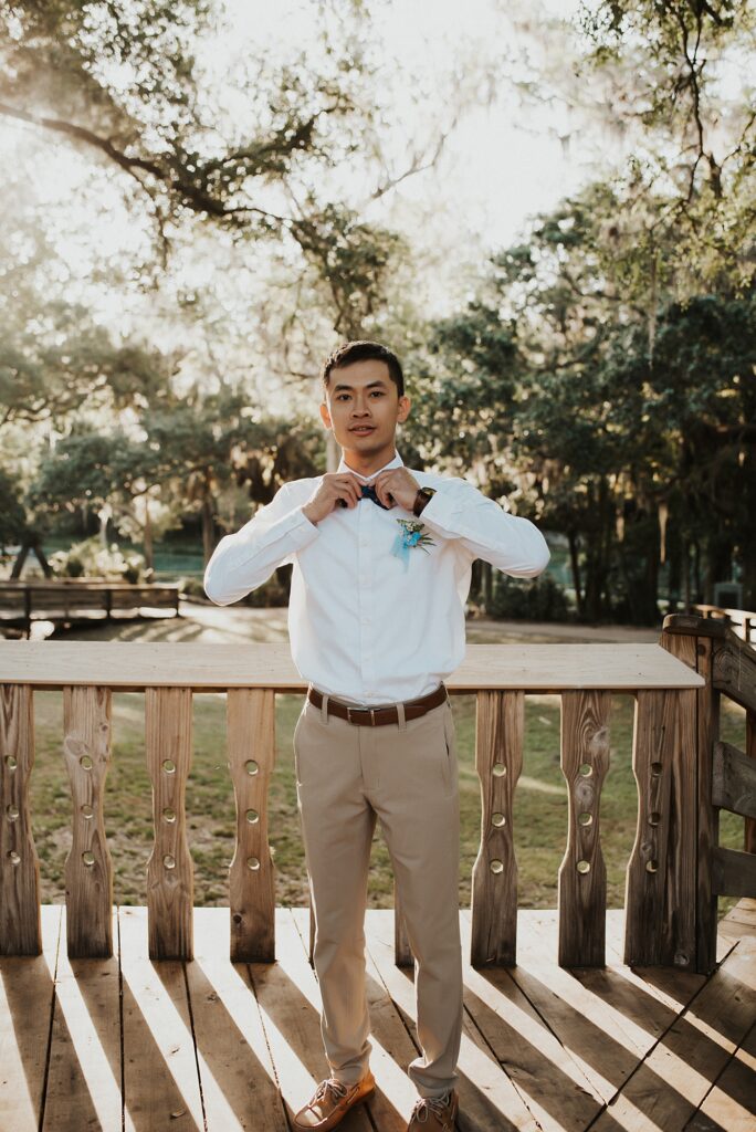 Groom fixing bowtie on a deck in spring