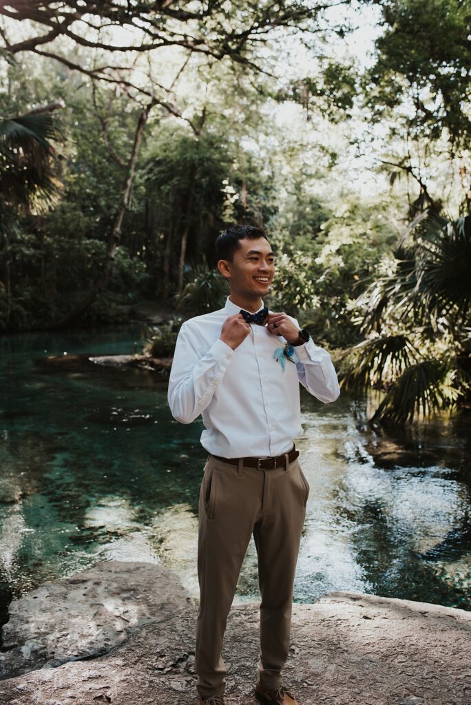 Groom fixing bowtie at Kelly Park Rock Springs in Apopka Florida during her elopement