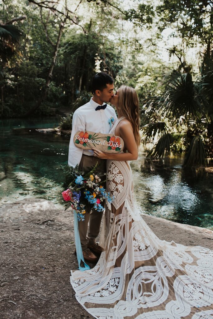 Bride and groom with permanent dibs elopement sign and spring floral bouquet at Kelly Park Rock Springs in Apopka Florida during her elopement