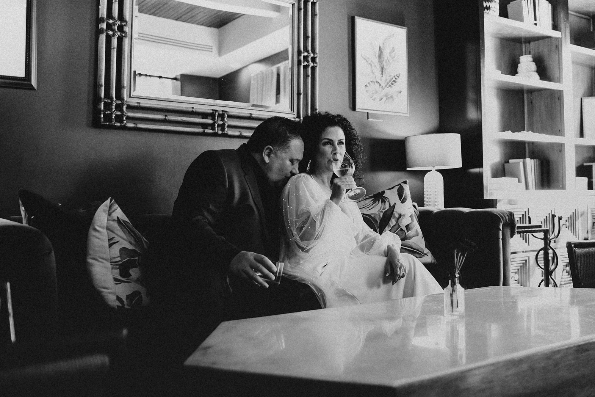 Bride and groom sitting on a couch as groom kisses brides shoulder