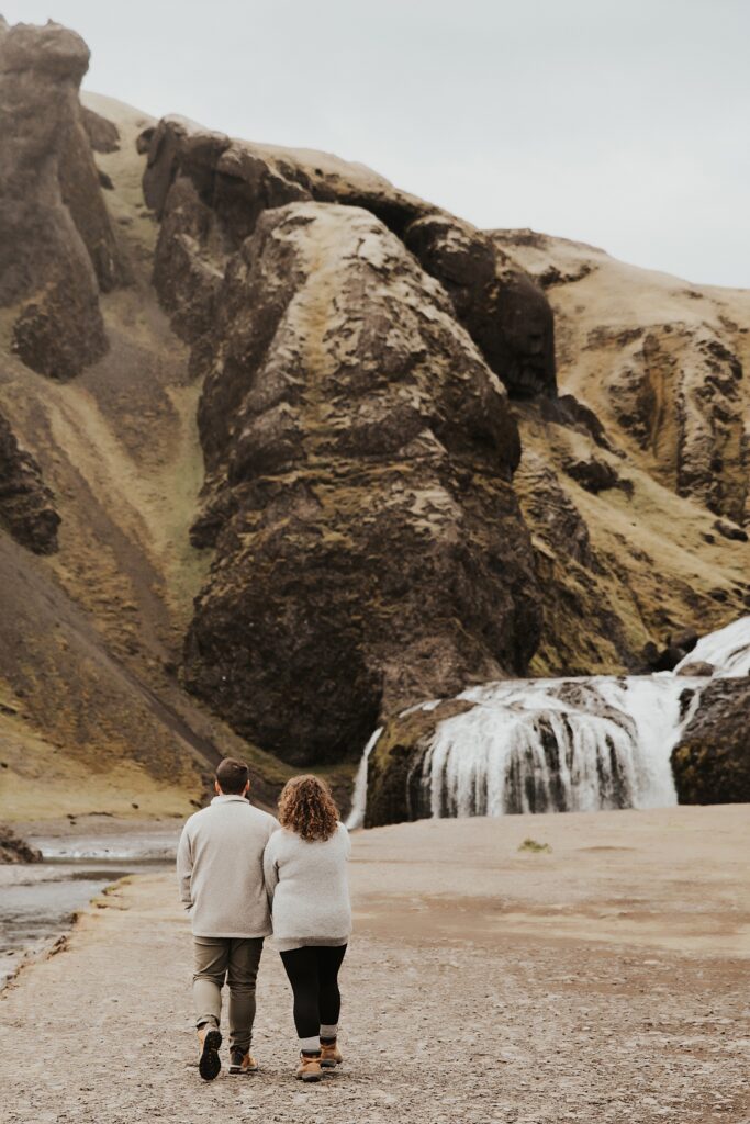 Couple holding hands and walking towards a waterfall