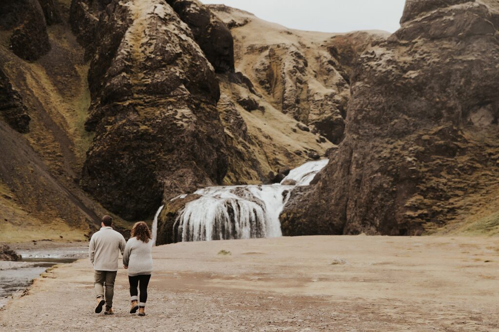 Couple holding hands and walking towards a waterfall