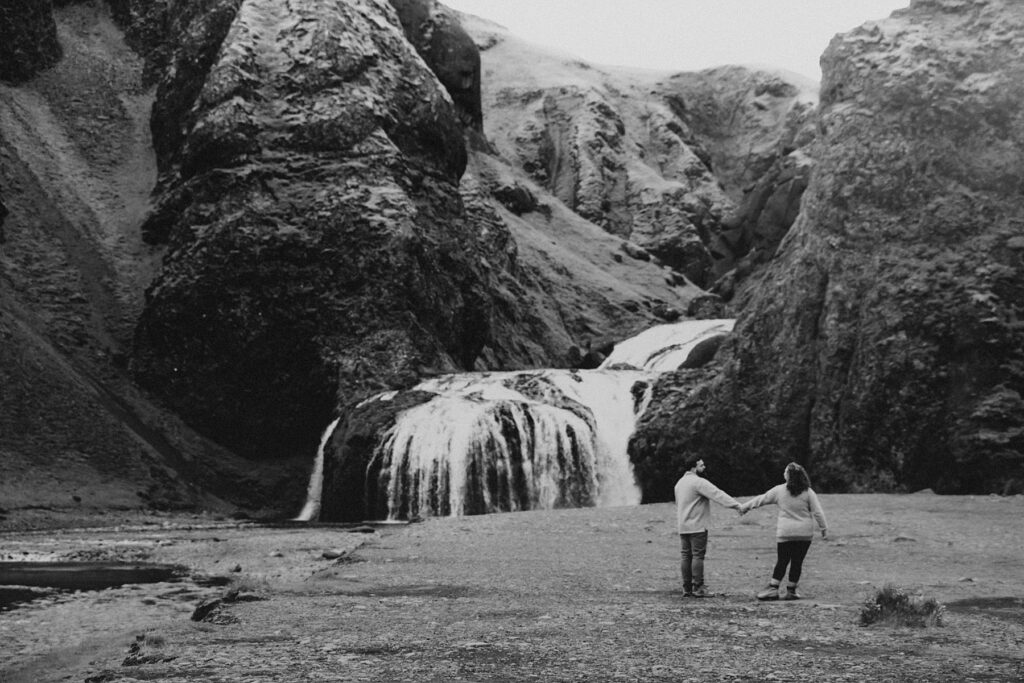 Couple holding hands and walking towards a waterfall